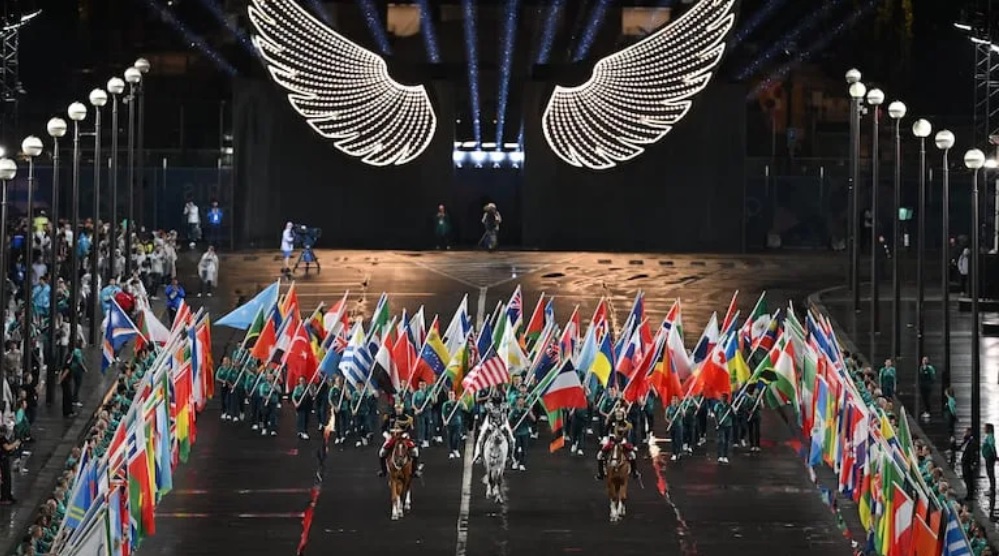 El caballero enmascarado lleva la bandera olímpica seguido por voluntarios que participaron de la ceremonia, de la Torre Eiffel a la plaza del Trocadero Foto cortesía EFE